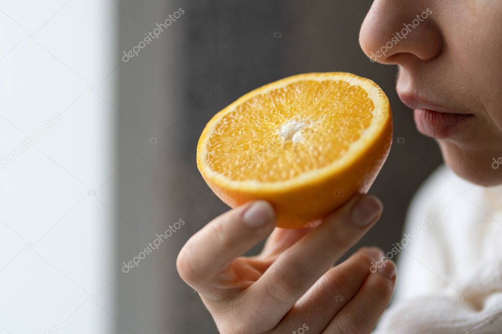 Sick woman trying to sense smell of half fresh orange, has symptom of Covid-19, loss of smell, taste