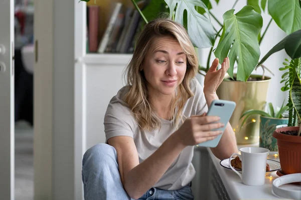 Vrouw houdt telefoon in handen, verrast door bericht, leest de kennisgeving met een lichte grijns — Stockfoto