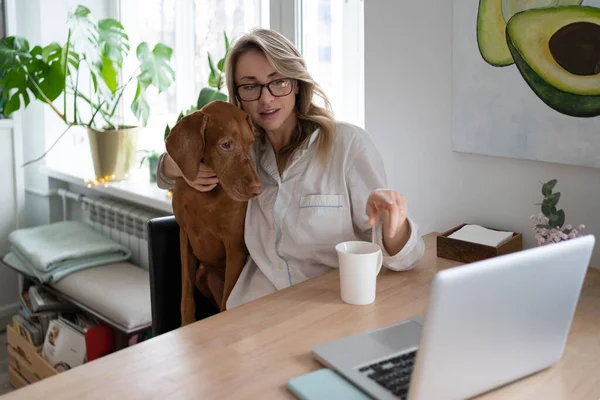 Lächelnde Frau umarmt ihren Vizsla-Hund, spricht im Videochat am Laptop und zeigt mit dem Finger auf den Bildschirm — Stockfoto