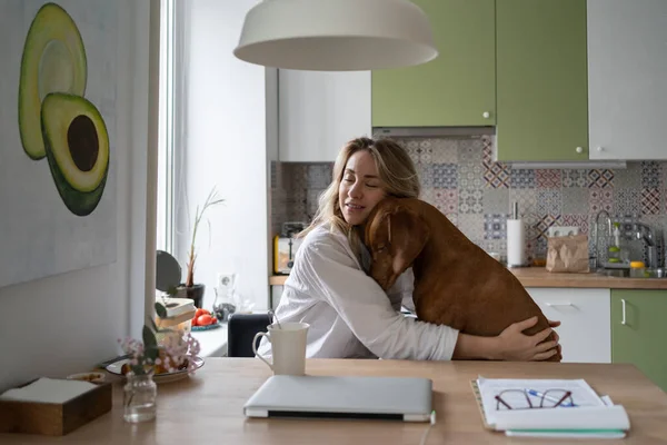 Žena ve spacáku objímající svého milovaného psa Wirehaired Vizsla, sedící na židli v kuchyni — Stock fotografie