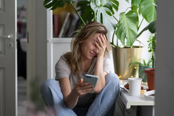 Žena dělá facepalm gesto, dotýká se dlaní hlavy, dívá se na telefon, poslal email na špatnou adresu — Stock fotografie