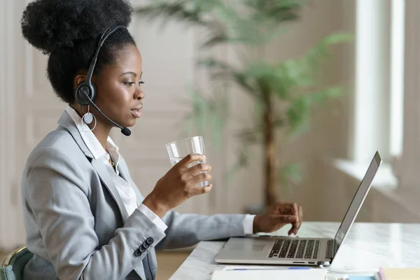 Afro empregado mulher olhando para tela do laptop, trabalhando em casa escritório, beber água de um copo. — Fotografia de Stock