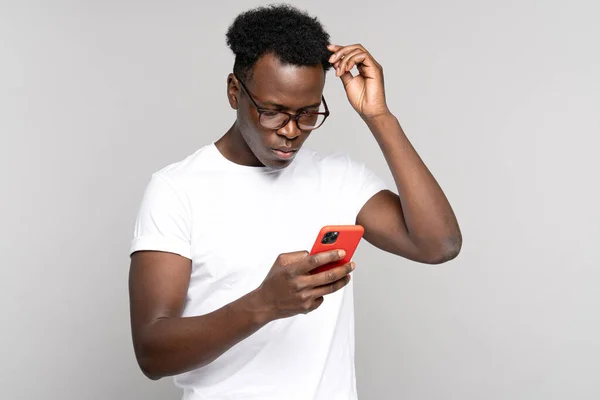 Pensive Afro homme se gratter la tête, en regardant le téléphone mobile, penser, plans ou reconsidère quelque chose — Photo