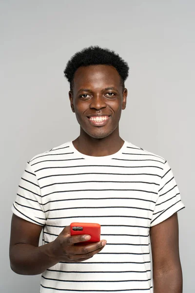 Feliz homem milenar Africano em óculos, segurando telefone celular, isolado no estúdio fundo cinza — Fotografia de Stock