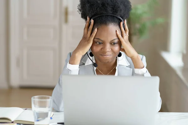 Enojada molesta mujer de negocios afro gritando, usar auriculares hablando con un mal trabajo de cliente en el ordenador portátil — Foto de Stock