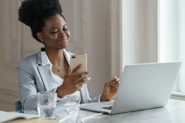 Souriant Afro femme prendre une pause bavarder avec un ami sur week-end dans les médias sociaux assis au bureau — Photo