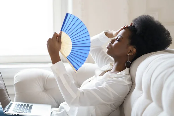 Afro-Geschäftsfrau, die an Hitzschlag leidet, sitzt mit wehendem Ventilator zu Hause im Wohnzimmer — Stockfoto
