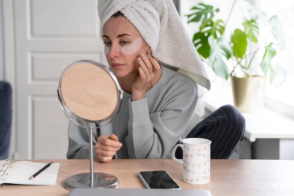 Mulher com toalha na cabeça aplicar hidrogel sob os olhos remendos de recuperação em casa, olhando no espelho. — Fotografia de Stock