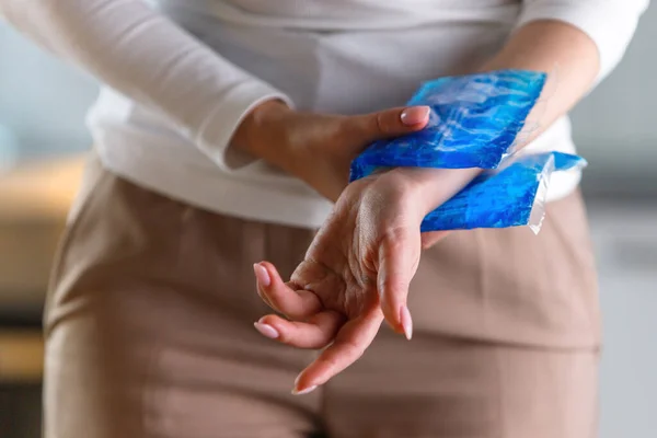 Close up of woman applying cold compress to a her painful wrist caused by prolonged work on the computer, laptop. Carpal tunnel syndrome, arthritis, neurological disease concept.