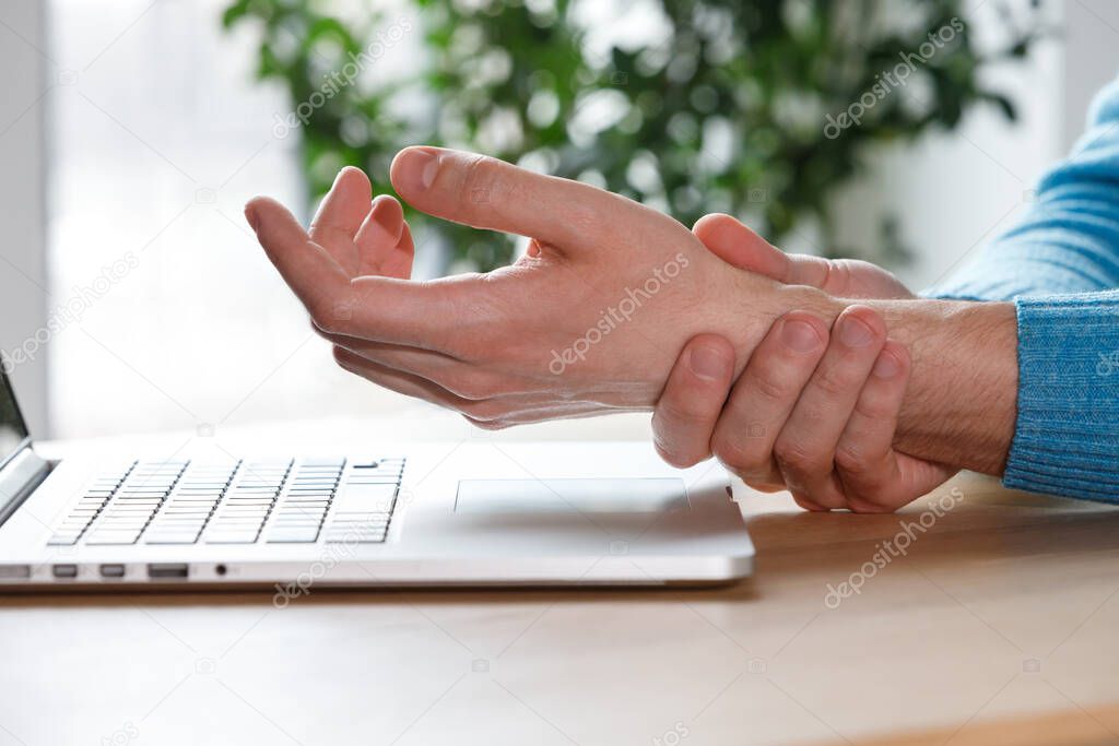 Close up of man arms holding his painful wrist caused by prolonged work on the computer, laptop. Carpal tunnel syndrome, arthritis, neurological disease concept. Numbness of the hand