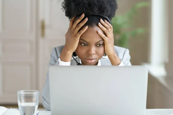 Trött irriterad afro kvinna bära hörlurar prata med en dålig klient tittar på skärmen laptop på kontoret — Stockfoto