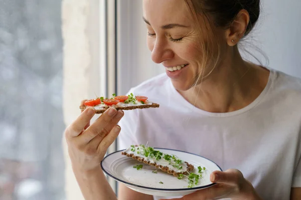 Çavdar ekmeği yiyen kadın kremalı vejetaryen peynirli tofu, domates, mikro yeşillikler. Sağlıklı yemek. — Stok fotoğraf