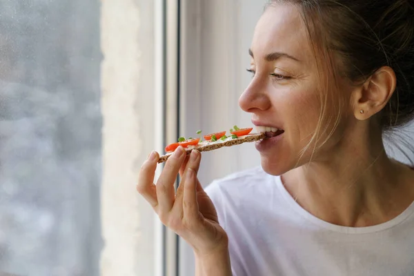 Kvinna äter rågknäckebröd med krämig vegetarisk ost tofu, tomat, mikrogröna. Hälsosam mat — Stockfoto