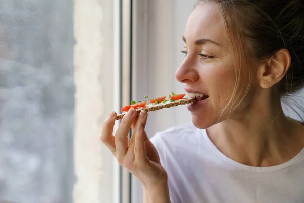 Mulher comendo pão crocante de centeio com tofu de queijo vegetariano cremoso, tomate, micro verdes. Alimentos saudáveis — Fotografia de Stock