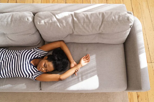 Mujer joven afroamericana usa camiseta desnuda descansando, durmiendo en el sofá con los brazos en casa —  Fotos de Stock