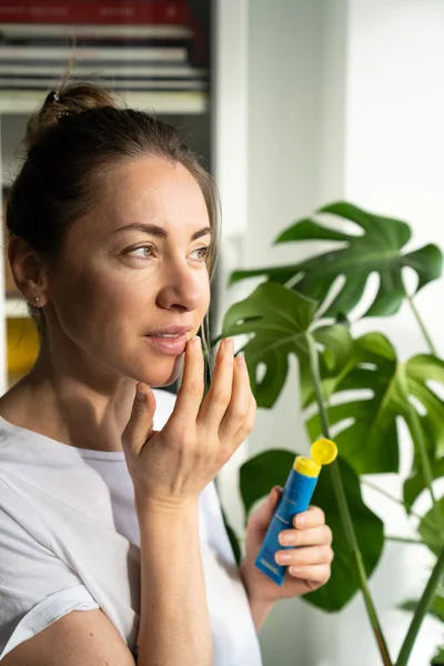 Frau trägt feuchtigkeitsspendenden Balsam auf ihre Lippen auf, um Trockenheit zu verhindern, in der kalten Jahreszeit rissig — Stockfoto