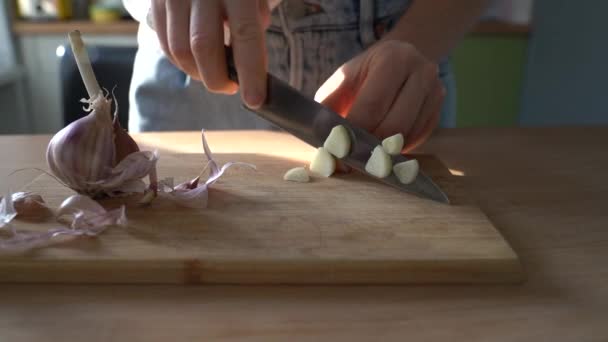 Închiderea brațelor femeii tăind usturoiul pe placa de lemn pentru gătit, stând în bucătăria ei de acasă . — Videoclip de stoc