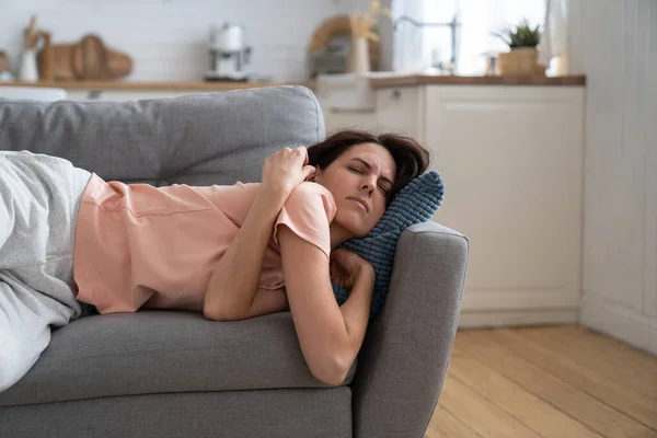 Woman with closed eyes lying on pillow resting trying to sleep in uncomfortable pose on sofa at home