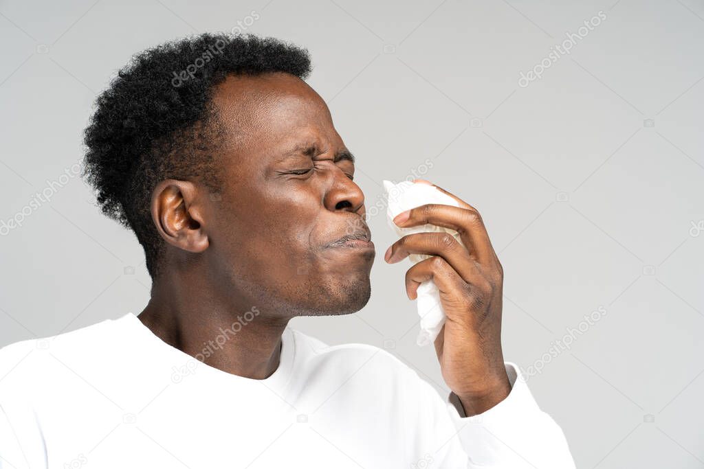Black man blowing nose and sneeze into tissue or napkin, has allergy, first symptoms of cold and flu