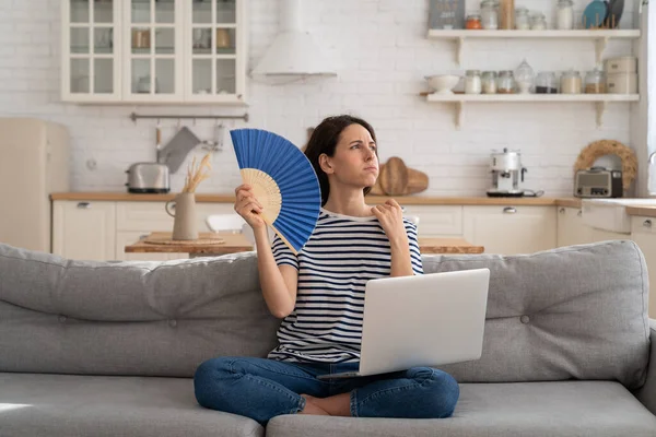 Jonge vrouw lijdt aan een hitteberoerte plat zonder airconditioner zwaaien ventilator zittend op de bank thuis — Stockfoto