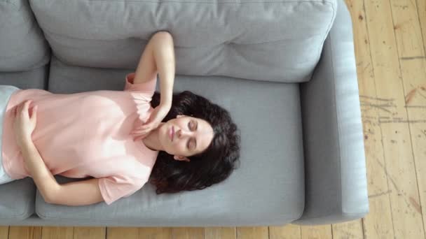 Junge Frau schläft auf Couch mit erhobenem Arm zu Hause, schließt die Augen und macht eine Pause, Draufsicht. — Stockvideo