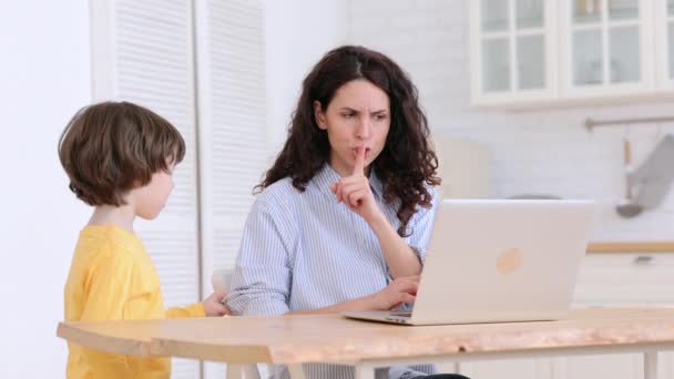 Mãe senta-se à mesa no escritório em casa durante o confinamento, trabalhando no laptop, criança distrai e fazendo barulho — Vídeo de Stock