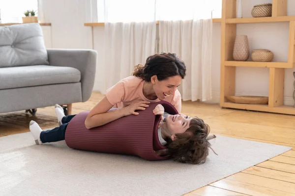 Mor insvept leende unge i yoga matta leka med son efter sport motion hemma under lockdown — Stockfoto