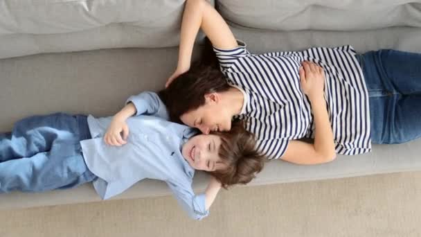 Пара беззаботных мать и милый ребенок лежит, отдыхая на диване весело смотрит вместе на камеру — стоковое видео