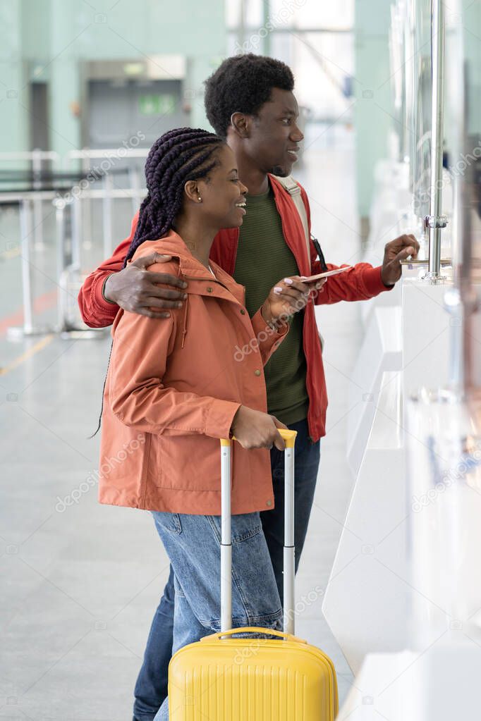 Happy African couple with foreign passports and boarding passes standing at airport check-in counter