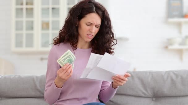 Сумна молода дівчина тримає останні готівкові гроші, відчуваючи тривогу щодо боргу або банкрутства, сидячи вдома . — стокове відео