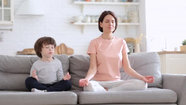 Mamma med söt liten son gör yoga motion sitta tillsammans på soffan hemma lära barn att meditera — Stockvideo