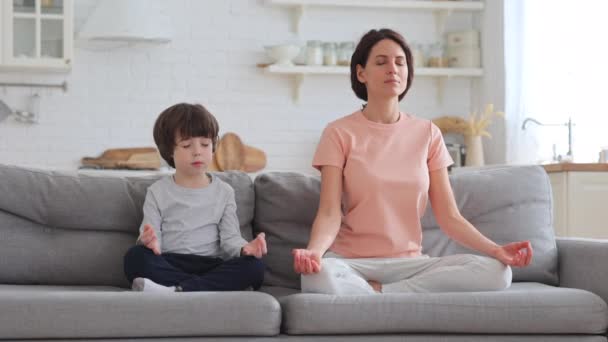 Ibu dengan anak kecil yang lucu melakukan latihan yoga duduk bersama di sofa di rumah mengajar anak-anak untuk bermeditasi — Stok Video