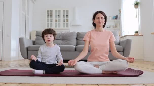 Mom with little son doing yoga exercise, practicing, teaching child to meditate, sit on mat at home. — Stock Video