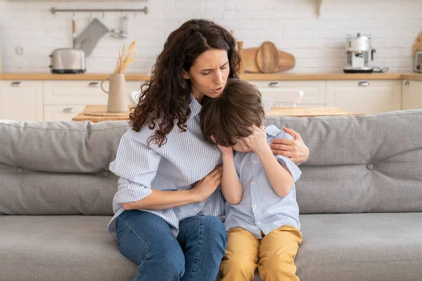 Young mother comfort crying son. Disturbed mom hug small upset preschool boy sitting in living room — Stock Photo, Image