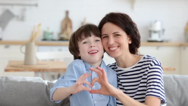 Mutter und Sohn machen Herz-Hand-Geste zusammen glücklich lächelnden Blick in die Kamera zu Hause auf dem Sofa sitzend — Stockvideo