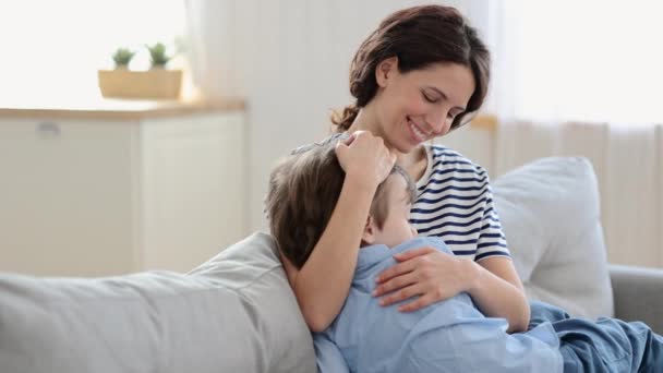 Feliz mãe abraço filho dormir de joelhos. Bonito mãe caucasiana e criança pré-escolar abraçar no sofá em casa — Vídeo de Stock