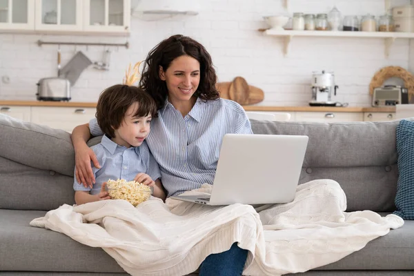 Smiling mother and little preschool son watch funny video, cartoon on laptop together in living room