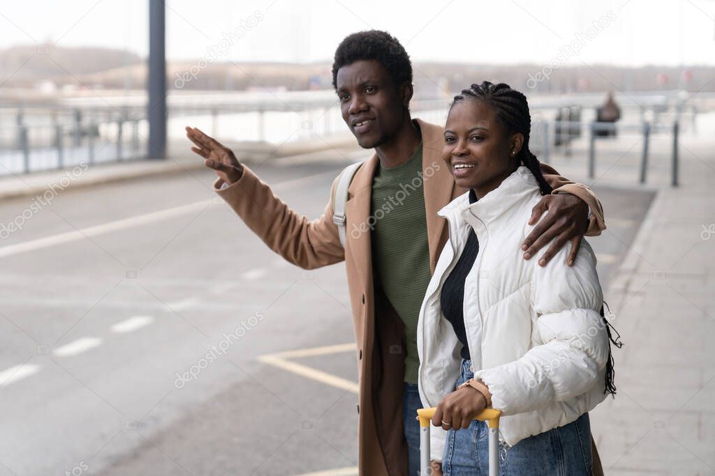 Transfer from terminal: african couple near airport with raised hand try to catch taxi after arrival