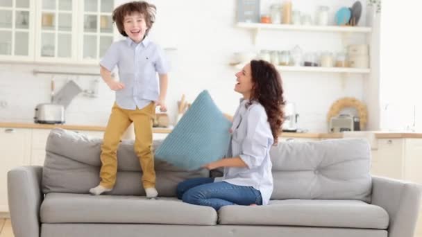 Anne ve oğlu oturma odasında yastıklarla kavga ederek eğleniyorlar. Aile eğlencesi ve eğlence zamanı. — Stok video