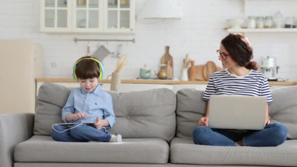 Mãe trabalho remoto freelancer de casa escritório no laptop sentar-se no sofá criança jogando no tablet. Bloqueio — Vídeo de Stock