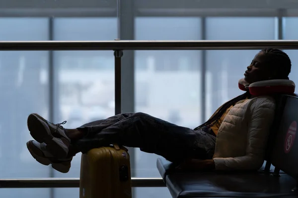 Tired woman sleep in airport on chair with legs on suitcase waiting for transit flight departure