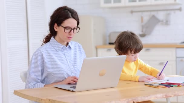 Koncentrovaná příležitostná obchodnice číst obchodní e-mail na notebooku v blízkosti malého syna z domácí kanceláře — Stock video