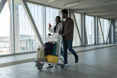 Happy African couple travel after coronavirus pandemic end. Black passengers in airport with luggage clipart