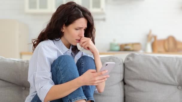 Mujer joven llorar leer malas noticias de correo electrónico, mensaje de ruptura ex-novio en el teléfono inteligente sentarse solo en el sofá — Vídeo de stock