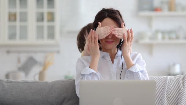 Moeder werk op laptop thuis tijdens lock-down, kind afleidt van het werk, het bedekken van haar moeders ogen — Stockvideo