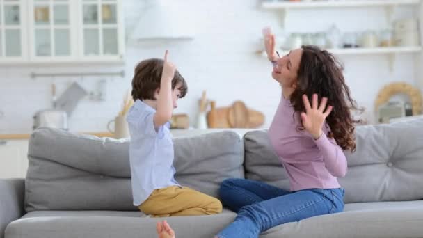 Lycklig mamma leker med sitt barn på soffan hemma, gör rolig grimace. Familj, förälder, kärlek. — Stockvideo