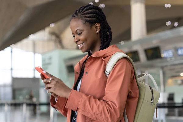 Mutlu afro kadın ilk uçuştan sonra havaalanına vardıktan sonra akıllı telefon mesajlarını kontrol et. — Stok fotoğraf