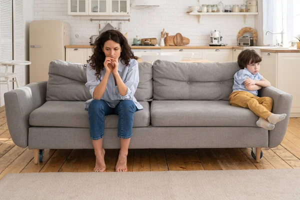 Offended mom and son sit on couch in living room avoid talking looking at each other after quarrel