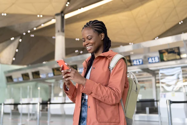 Mutlu afro kadın ilk uçuştan sonra havaalanına vardıktan sonra akıllı telefon mesajlarını kontrol et. — Stok fotoğraf