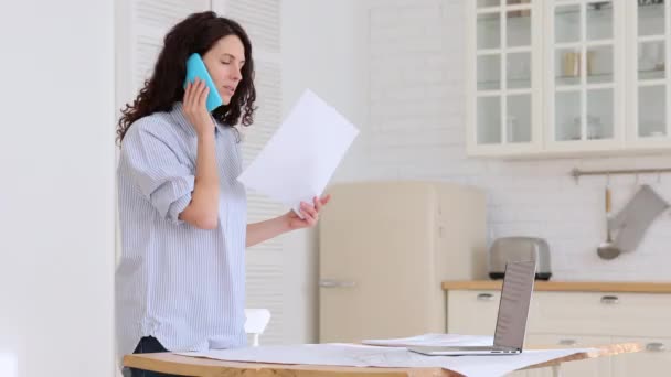 Mulher segurando documentos falando no celular trabalho remoto do escritório em casa durante o bloqueio vívido — Vídeo de Stock